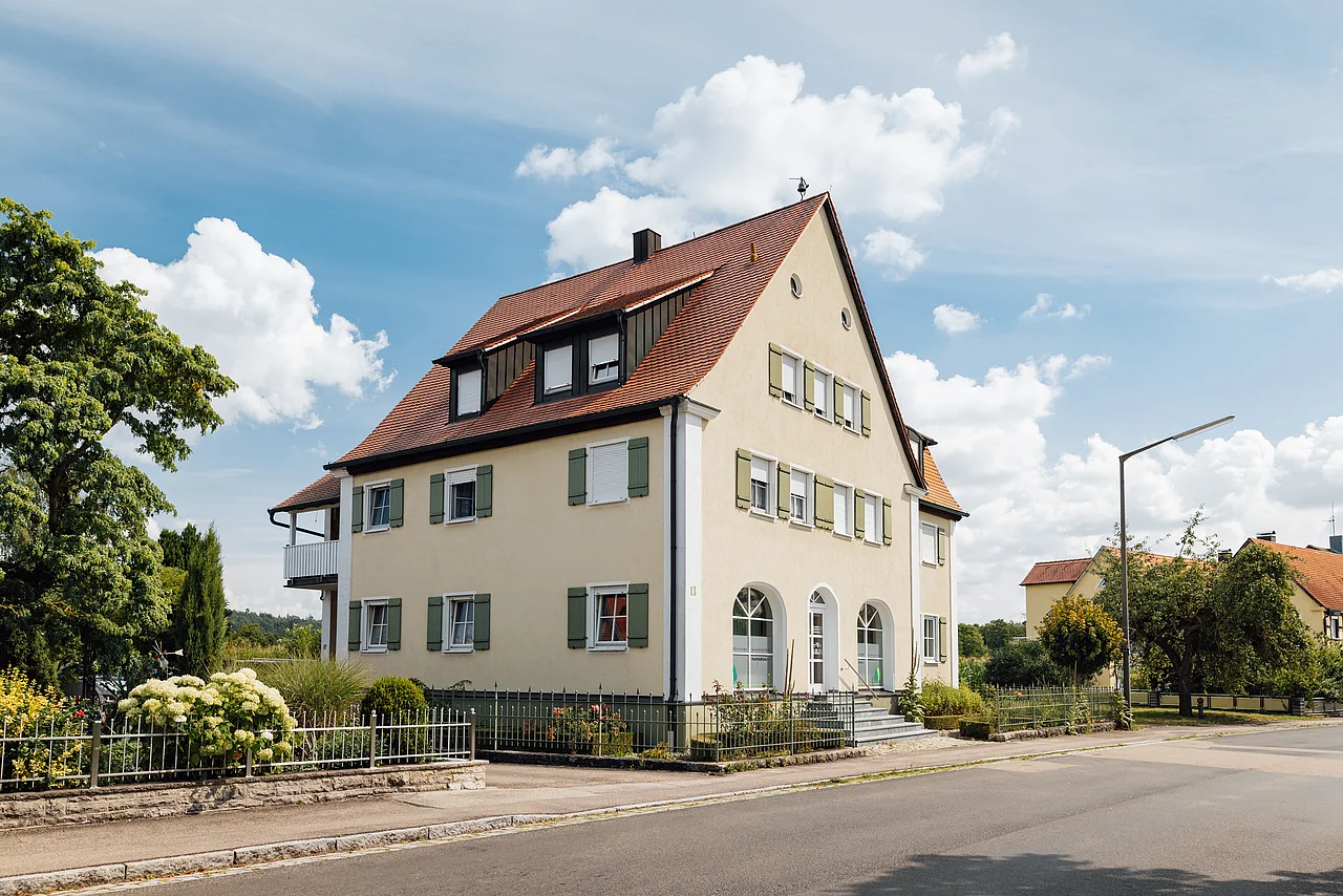 Gebäude der FBG Westmittelfranken mit hellem Putz und rotem Dach an einer Straße.
